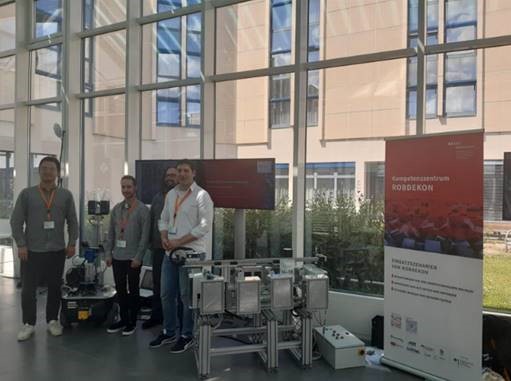 Gruppe vor Technik-Exponaten und Roll-Up des Kompetenzzentrums RODEKON in lichtdurchflutetem Raum.